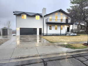 View of front of house with a balcony, driveway, an attached garage, an outdoor structure, and a storage shed