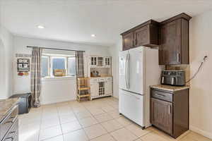 Kitchen featuring light tile patterned floors, recessed lighting, freestanding refrigerator, dark brown cabinets, and baseboards