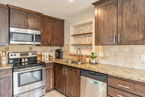 Kitchen with light stone countertops, tasteful backsplash, stainless steel appliances, and a sink