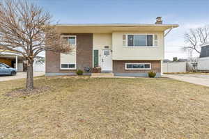 Bi-level home with a front yard, brick siding, fence, and a chimney