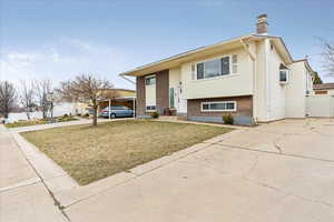 Raised ranch with brick siding, a chimney, a front yard, fence, and driveway