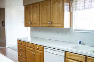 Kitchen with white dishwasher, a sink, baseboards, light countertops, and brown cabinets