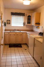 Kitchen featuring a sink, washer and clothes dryer, a textured ceiling, and light brown cabinetry