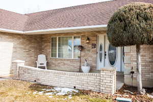 View of exterior entry with a shingled roof and brick siding