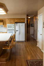 Kitchen with white appliances, baseboards, dark wood-style flooring, light countertops, and a textured ceiling