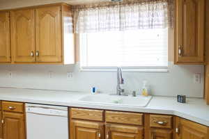 Kitchen featuring dishwasher, light countertops, brown cabinetry, and a sink