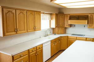 Kitchen with black electric stovetop, a sink, light countertops, dishwasher, and brown cabinetry