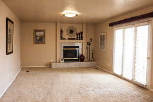 Unfurnished living room with plenty of natural light, carpet, a premium fireplace, and a textured ceiling