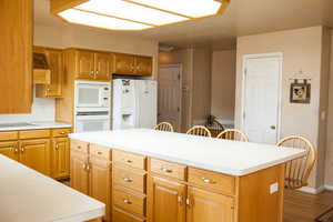 Kitchen featuring white appliances, a kitchen island, wood finished floors, baseboards, and light countertops