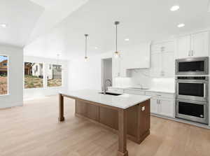 Kitchen featuring appliances with stainless steel finishes, light wood finished floors, recessed lighting, backsplash, and light stone countertops
