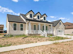 View of front facade with covered porch, stone siding, concrete driveway, a garage, and a shingled roof