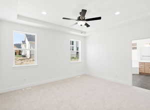 Unfurnished room featuring a raised ceiling, light colored carpet, a ceiling fan, and recessed lighting
