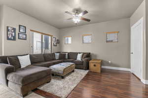 Living room with a ceiling fan, baseboards, and dark wood-type flooring
