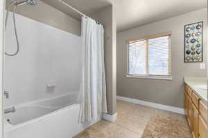 Full bathroom featuring a textured ceiling, vanity, baseboards, tile patterned floors, and shower / bath combo with shower curtain