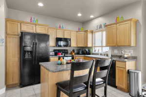 Kitchen featuring light brown cabinets, a sink, a kitchen breakfast bar, a center island, and black appliances