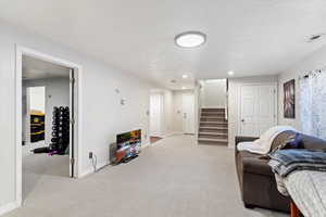 Carpeted living room featuring a textured ceiling, recessed lighting, visible vents, baseboards, and stairway