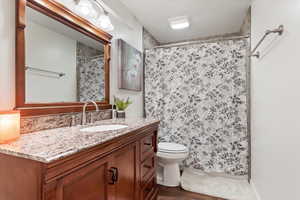 Full bathroom with toilet, curtained shower, wood finished floors, and vanity