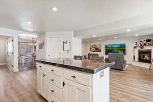 Kitchen with light wood finished floors, arched walkways, a glass covered fireplace, a center island, and recessed lighting