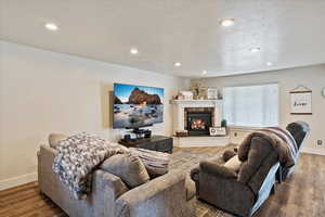 Living area with a fireplace, a textured ceiling, baseboards, and wood finished floors