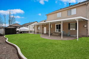 Rear view of house with entry steps, a storage shed, a lawn, an outdoor structure, and a patio area