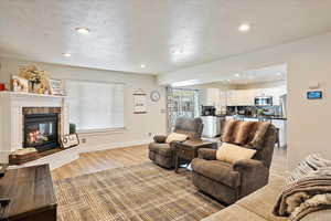 Living area featuring light wood-style flooring, a textured ceiling, baseboards, and a tiled fireplace