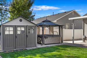 View of shed with fence, a hot tub, and a gazebo