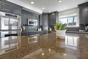 Kitchen featuring stainless steel appliances, dark stone countertops, and backsplash