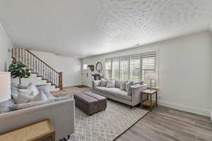 Living area featuring a textured ceiling, stairway, wood finished floors, and ornamental molding
