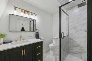 Full bath with toilet, marble finish floor, a stall shower, and vanity
