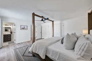 Bedroom with ensuite bathroom, a textured ceiling, multiple closets, ornamental molding, and light wood-type flooring