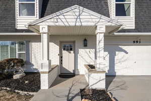 Doorway to property featuring an attached garage, brick siding, a porch, and roof with shingles