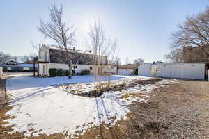 Snow covered back of property featuring a garage, stucco siding, and an outbuilding