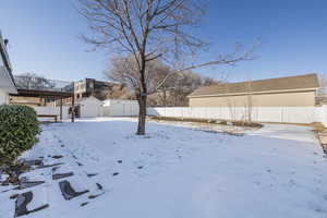 Yard covered in snow with a garage, a fenced backyard, a storage unit, and an outbuilding