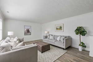 Living room featuring a textured ceiling, wood finished floors, visible vents, baseboards, and ornamental molding