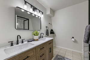 Bathroom with baseboards, double vanity, a sink, and tile patterned floors