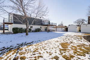 Snow covered house with a garage, a balcony, brick siding, and an outbuilding
