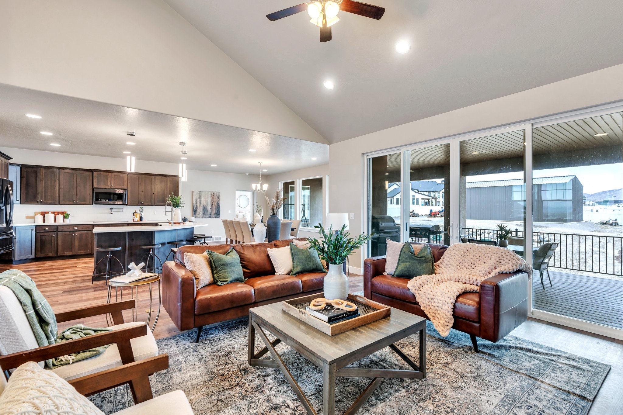Living room with high vaulted ceiling, a wealth of natural light, light wood finished floors, and ceiling fan with notable chandelier