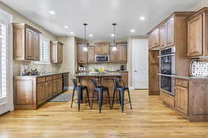 Kitchen featuring light wood-style flooring, a kitchen island, appliances with stainless steel finishes, brown cabinets, and a sink