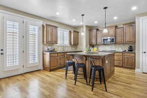 Kitchen featuring light wood-style flooring, a kitchen island, appliances with stainless steel finishes, brown cabinets, and a breakfast bar area