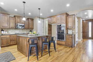 Kitchen featuring arched walkways, light wood-style flooring, light stone counters, a center island, and stainless steel appliances