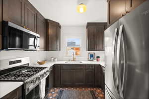 Kitchen featuring stainless steel appliances, light countertops, a sink, dark brown cabinetry, and dark tile patterned flooring