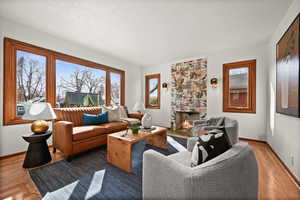 Living room featuring baseboards, a textured ceiling, a tiled fireplace, and wood finished floors