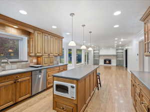 Kitchen with white microwave, a sink, a lit fireplace, light wood-type flooring, and dishwasher