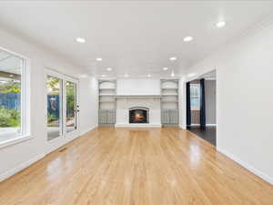 Unfurnished living room featuring crown molding, light wood-style floors, baseboards, and built in features