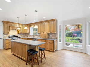 Kitchen with stainless steel gas stove, light wood finished floors, decorative backsplash, and a center island