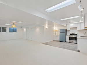 Kitchen with light carpet, stainless steel gas range oven, white cabinets, and freestanding refrigerator