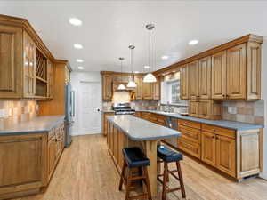 Kitchen featuring a breakfast bar, a sink, appliances with stainless steel finishes, a center island, and brown cabinetry