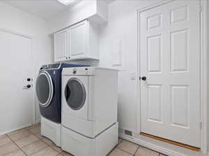 Washroom with light tile patterned floors, cabinet space, visible vents, baseboards, and separate washer and dryer