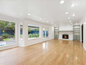 Unfurnished living room with light wood-style flooring, recessed lighting, a fireplace, built in features, and ornamental molding