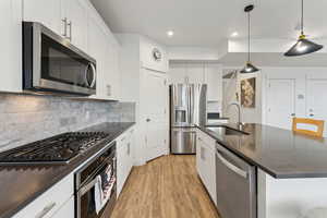 Kitchen with decorative backsplash, dark countertops, light wood-style flooring, stainless steel appliances, and a sink